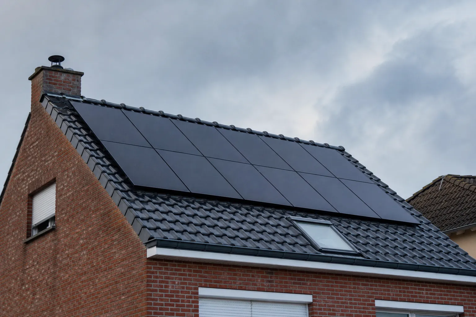 Toiture résidentielle nordiste en briques et ardoise avec une rangée de panneaux photovoltaïques posés, ciel nordique nuageux