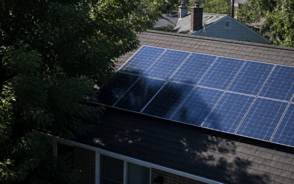 Toiture avec une rangée de panneaux photovoltaïques partiellement sous l’ombre portée d’arbres proches